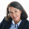 Smiling middle-aged woman with dark hair wearing a navy blazer and light blue shirt.